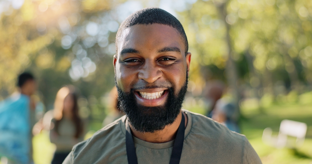 Black man, portrait and smile in park for charity, volunteer and community service work with donation. African person, happy and eco friendly outdoor for change, project and sustainability with NGO