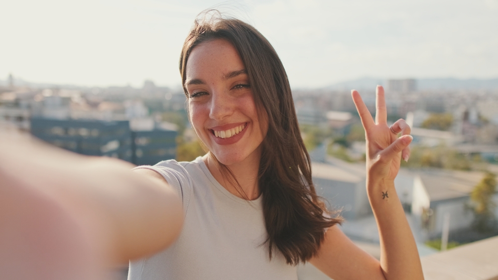 Close-up of young woman taking selfie hand peace sign while standing on balcony