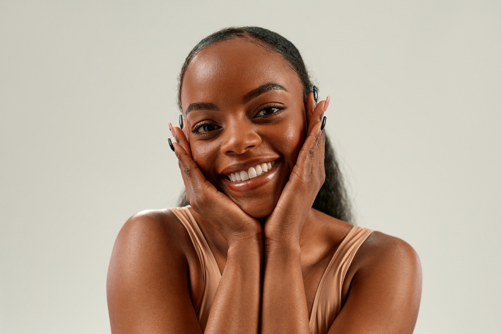 Scotts Valley Dental Patient Joyful young African American woman smiling brightly, gently cupping face with hands, expressing skincare, beauty, cosmetology concept.