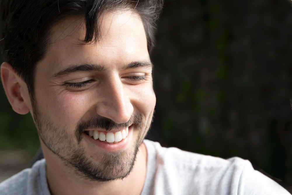 Cosmetic Dentistry for the Santa Cruz Community Portrait of a man laughing happily with a big casual smile on the street looking out. Beautiful smile of excited young man with perfect white teeth. Close up portrait of cheerful handsome man.